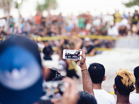 Image featuring a man holding his phone up to record something in a crowd.