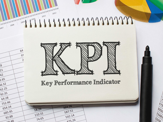 A pad with the words KPI, Key Permformance Indicators with a pen and sitting on a pile of charts and graphs.