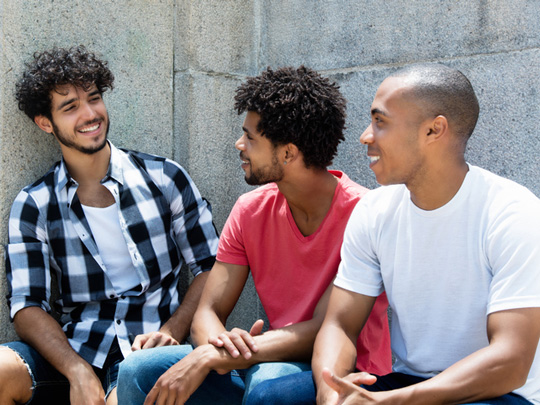 Three men sit on a bench joking together.