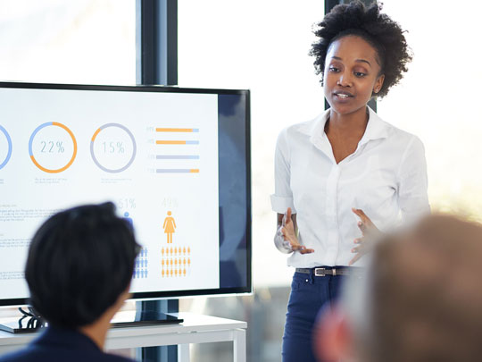 A woman presents metrics to two colleagues